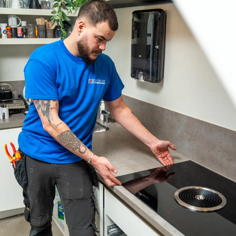 Elektricien van Louwmans wijst op een inductiekookplaat in een keuken
